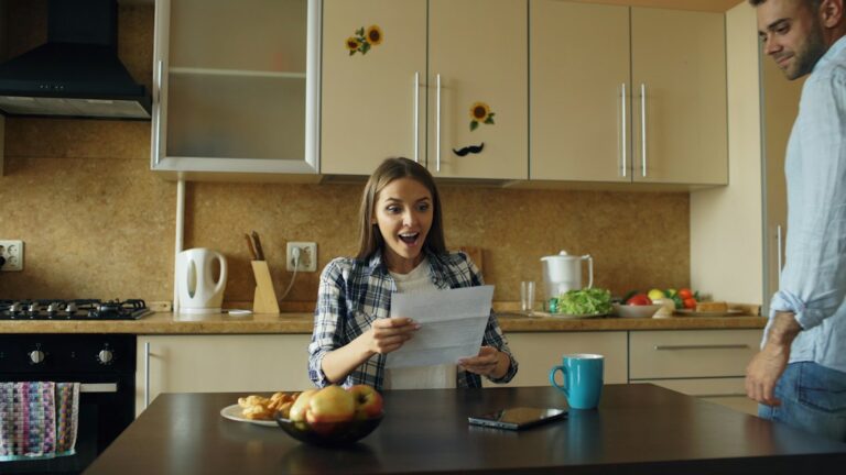 Couple reviews life insurance papers and household expenses at a kitchen table with a calculator.